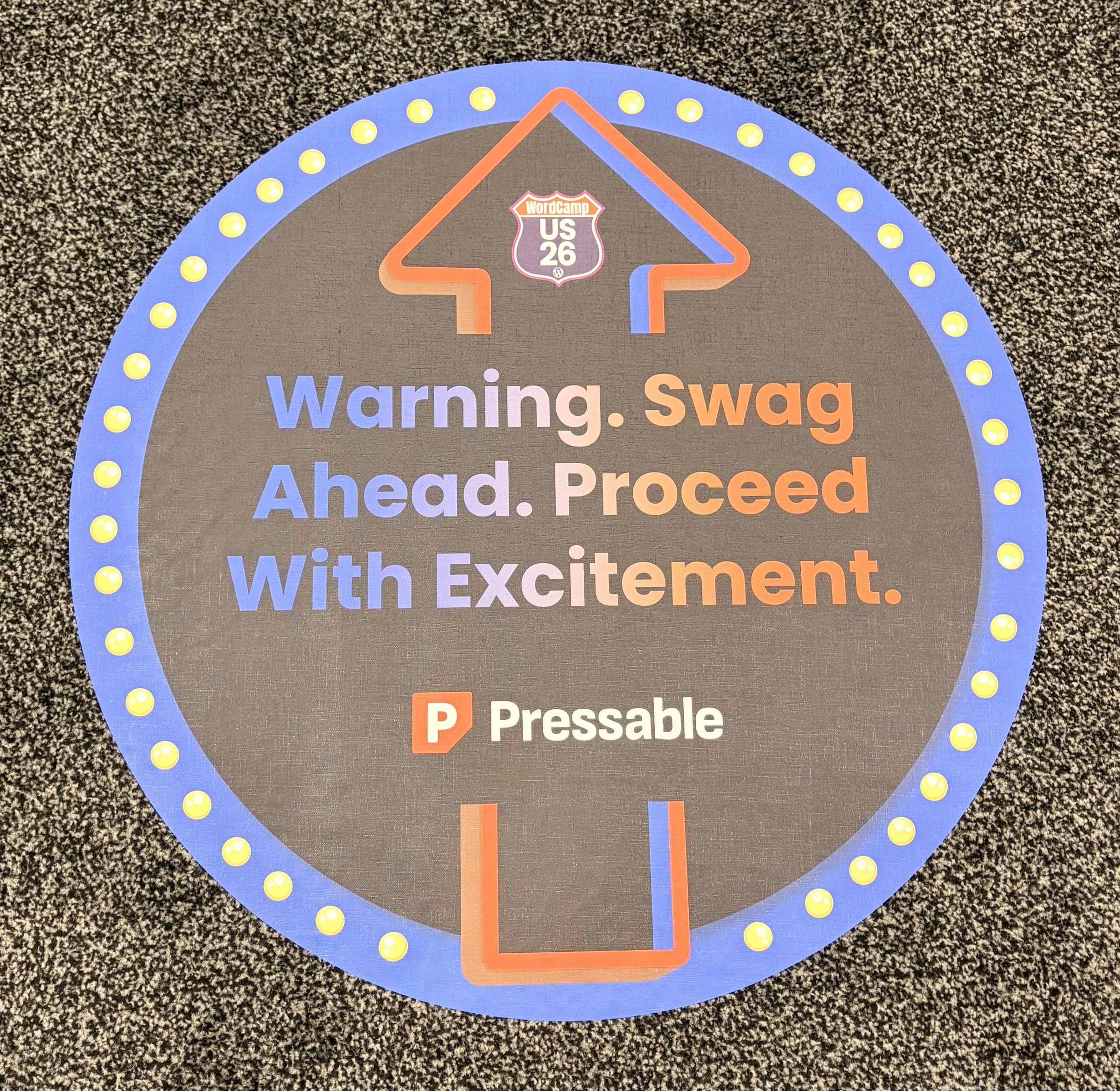 A round floor decal at WordCamp US that reads Warning. Swag Ahead. Proceed With Excitement.